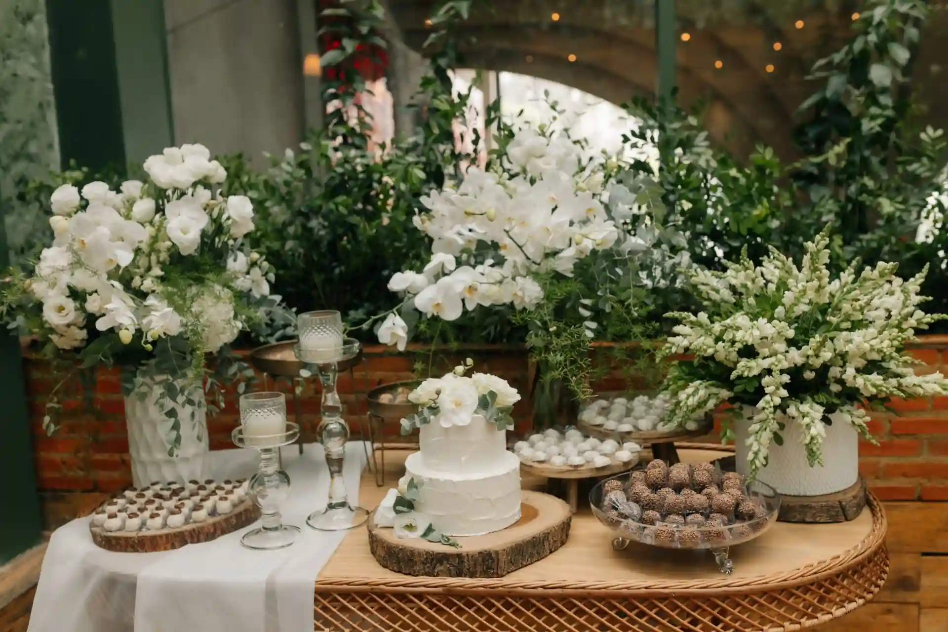 Decoração de festa com arranjos de flores brancas, bolo de bodas e doces em uma mesa de madeira, ideal para comemorações elegantes.