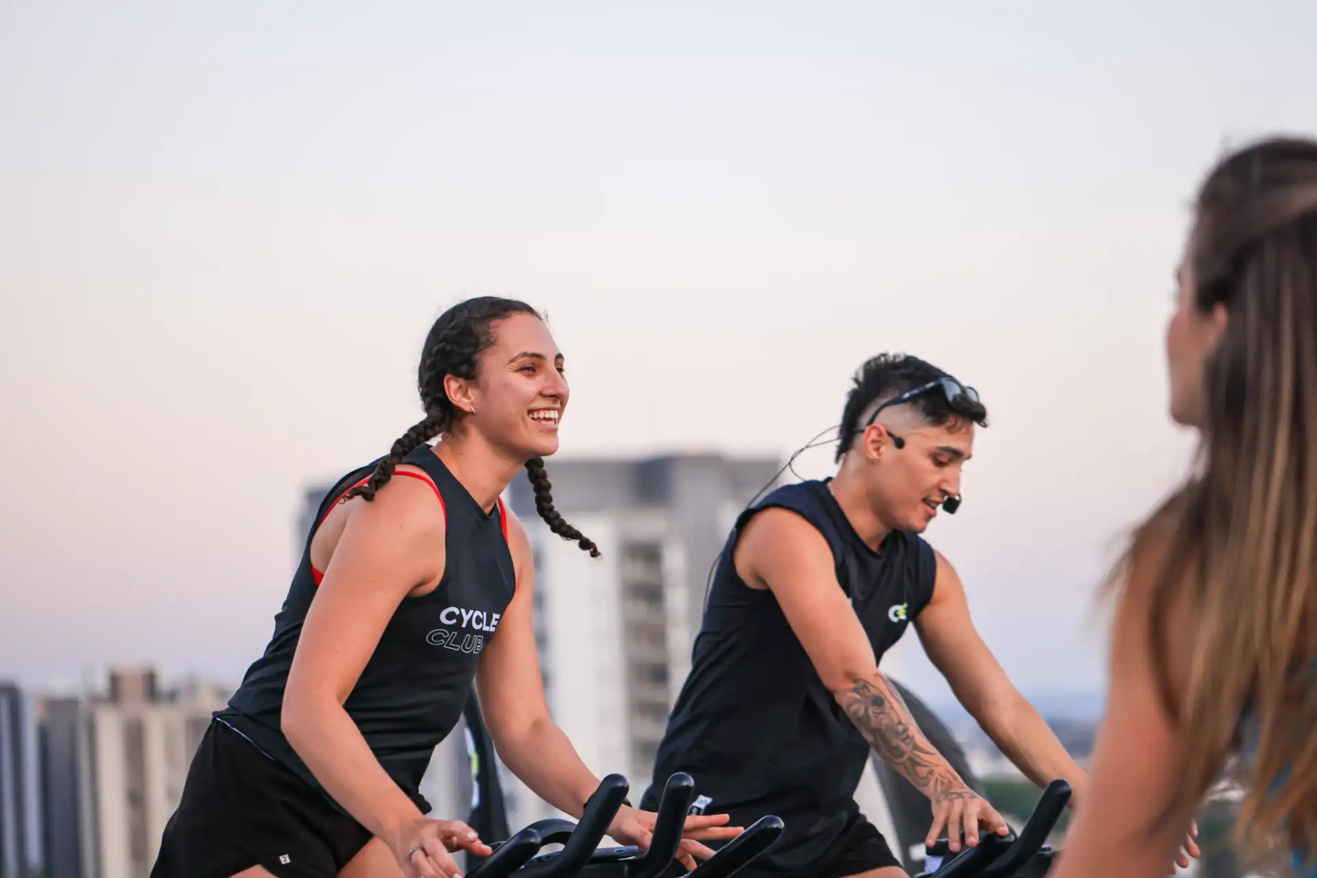 Grupo de pessoas praticando spinning ao ar livre em uma cidade, sorrindo e se divertindo durante o treino