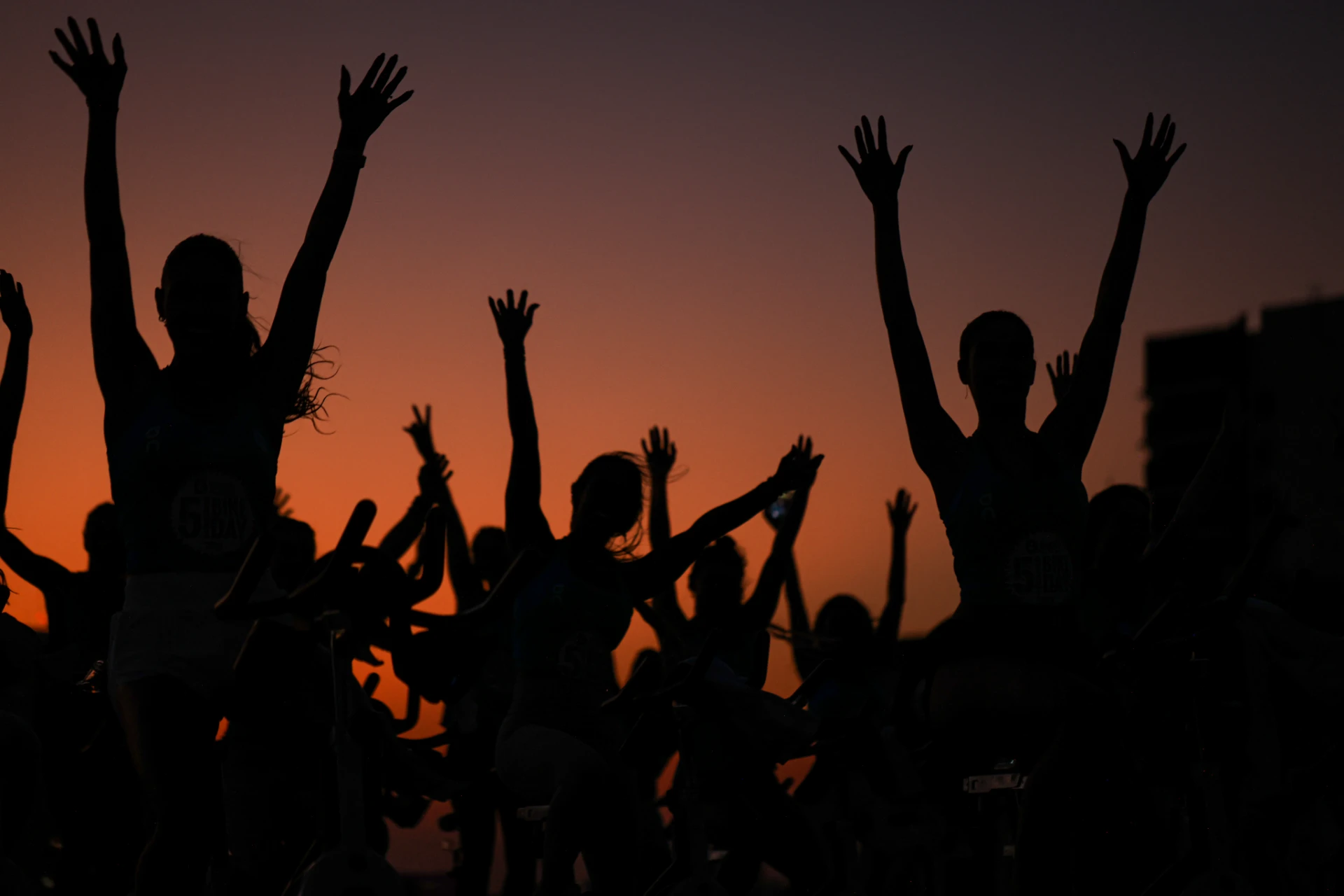atletas em spinning comemorando ao pôr do sol com os braços levantados em um ambiente ao ar livre, celebrando a amizade e a felicidade.