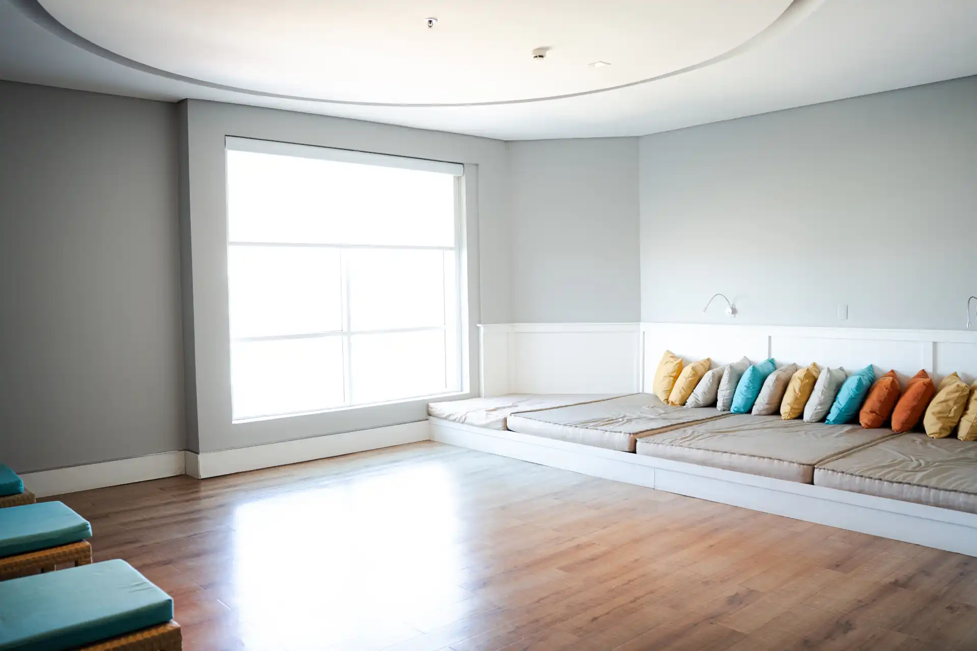 Sala de estar moderna com sofá baixo e almofadas coloridas, grande janela de vidro permitindo entrada de luz natural, piso de madeira, decoração minimalista