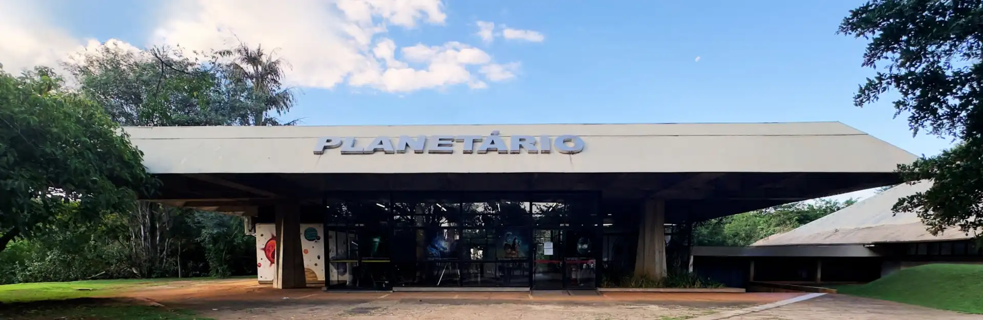 Imagem do Planetário, um espaço dedicado à astronomia, com arquitetura moderna e vista exterior com céu azul e árvores ao redor.