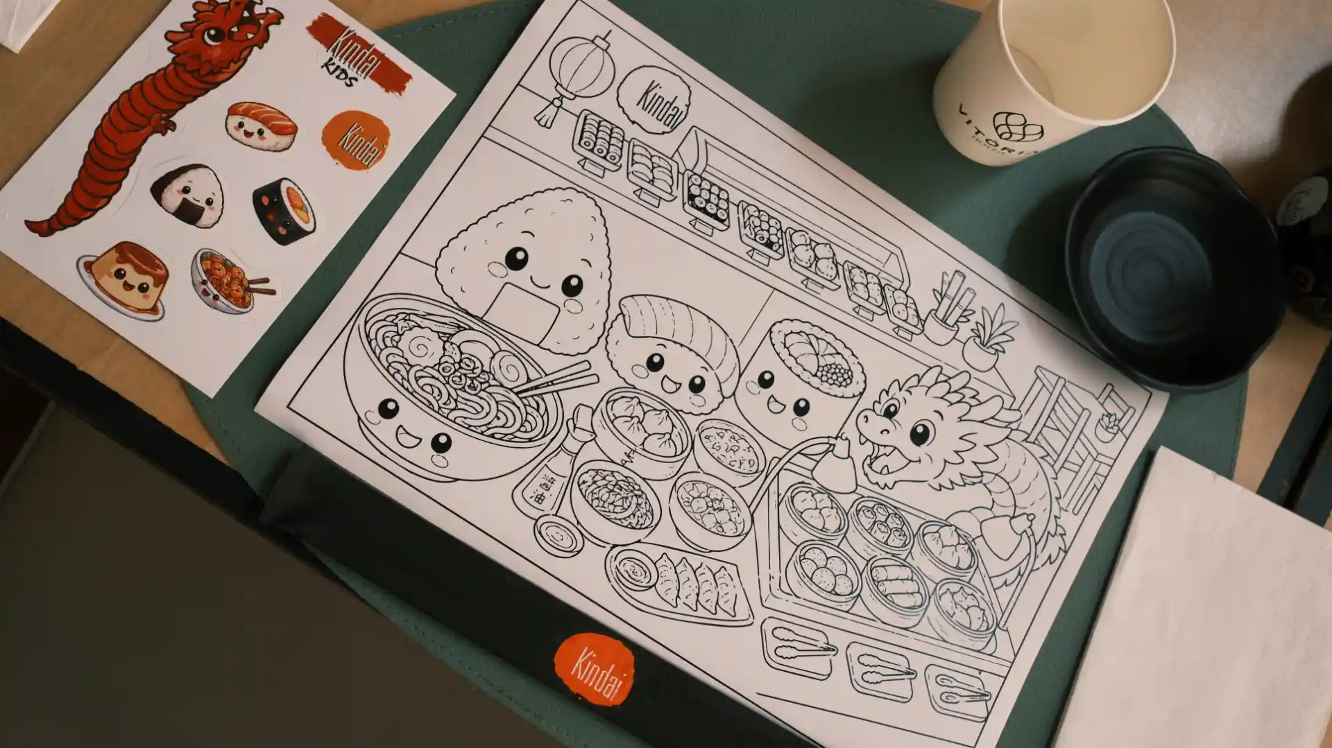 Imagem de uma atividade de colorir infantil com tema de culinária japonesa, incluindo personagens fofos de alimentos, utensílios e ingredientes em um ambiente de cozinha.