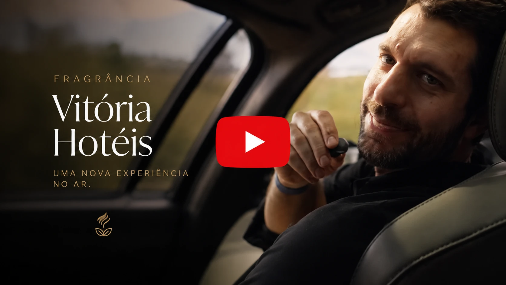 Homem ao volante dentro de um carro, segurando o celular no ouvido, com arte de divulgação de fragrância “Vitória Hotéis” e vídeo com botão play no centro da imagem.