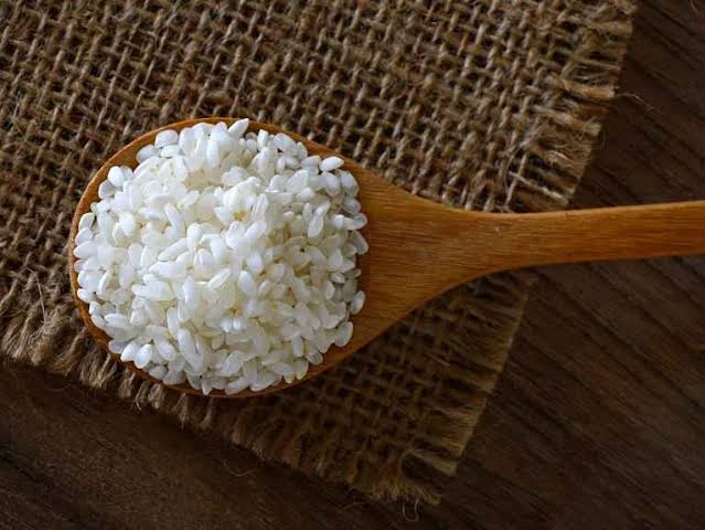 Colher de madeira com arroz gohan sobre tecido rústico, destacando a textura do ingrediente e o contraste entre a colher e o fundo.