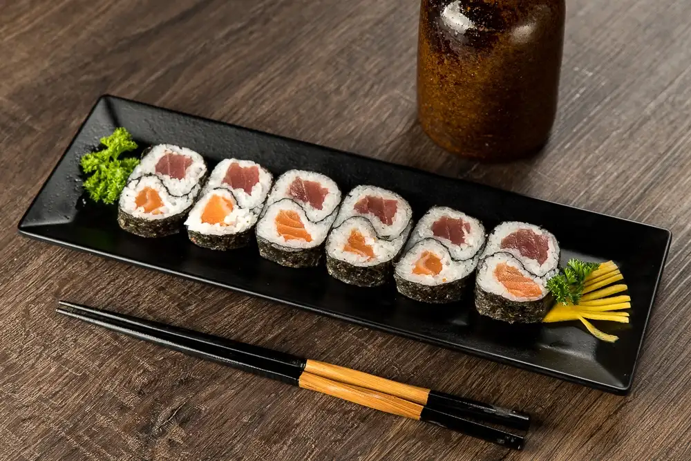 hossomaki variados em bandeja preta acompanhados de wasabi, gengibre em conserva e hashi sobre mesa de madeira