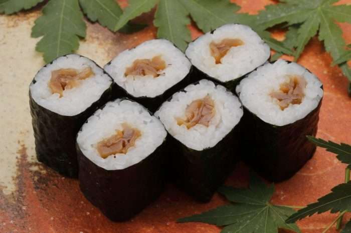 hossomaki com rolinhos de abóbora e arroz cobertos por alga nori, em uma bandeja rústica com folhas verdes e fundo laranja