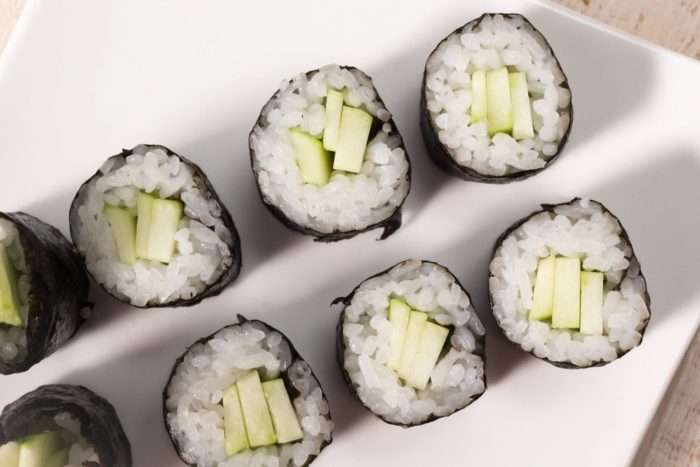 hossomaki enrolado em fatias de pepino com arroz branco, servido em uma travessa branca, com vários rolinhos dispostos em fila para apresentação gastronômica.
