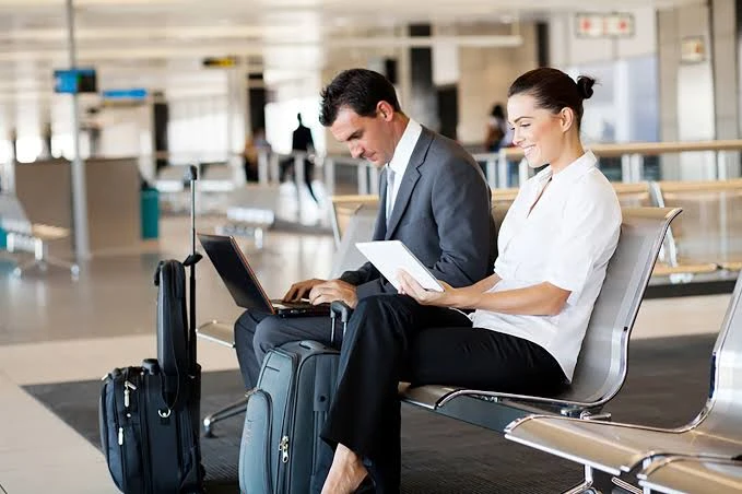 Homem e mulher em aeroporto com malas e documentos, analisando papéis e usando notebook em um ambiente de embarque.