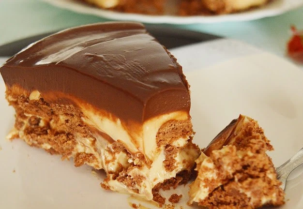 Fatias de sobremesa com doce de leite, com cobertura de chocolate escuro e recheio cremoso branco, com pedaços crocantes, servidas em prato com fundo desfocado.