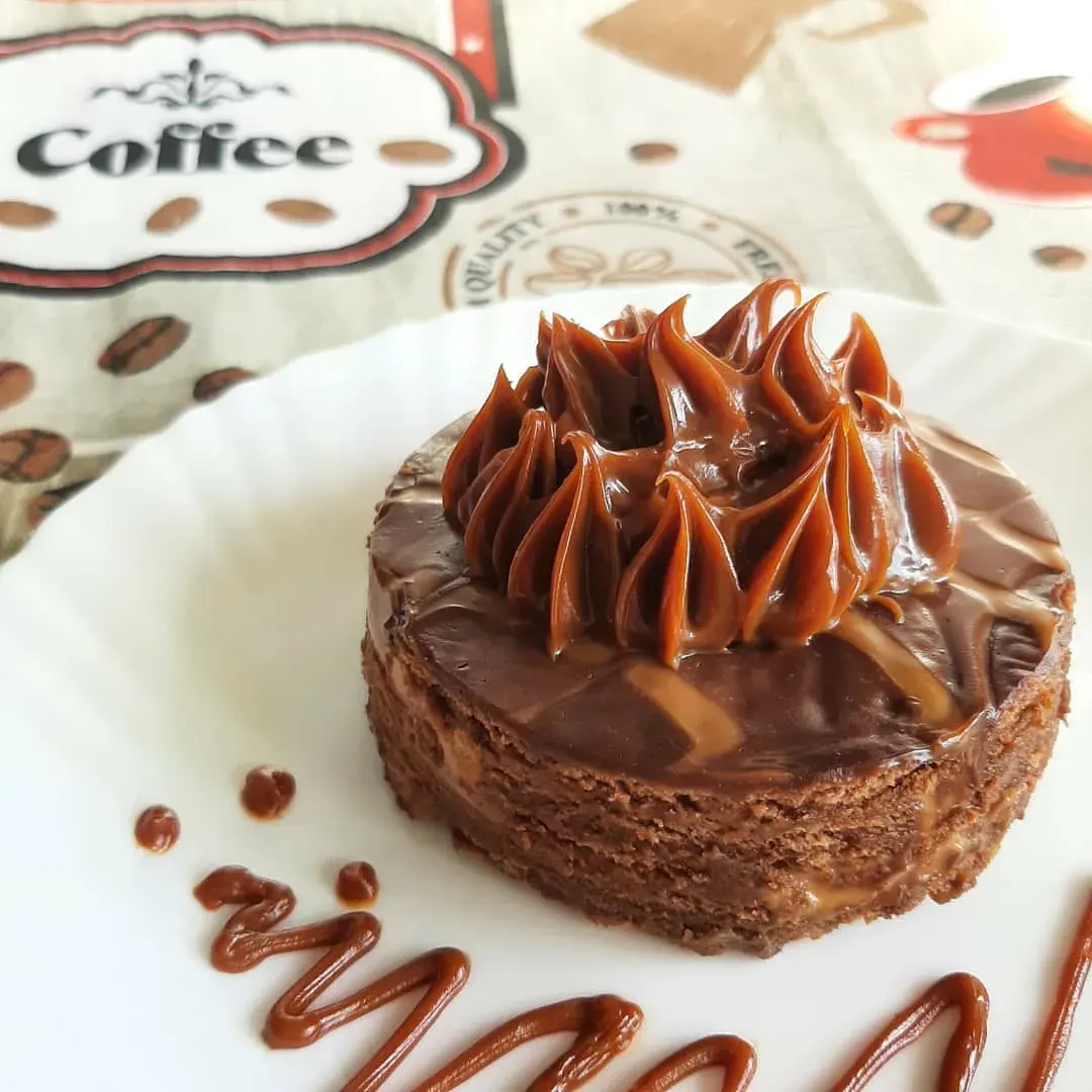 Torta individual de doce de leite com cobertura cremosa e cobertura de chocolate em formato de tiras, servida em prato decorado com grãos e o logo Coffee.